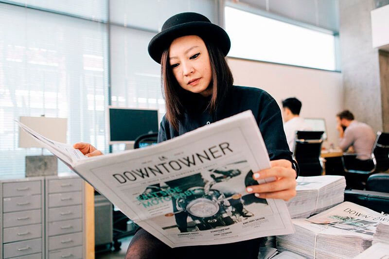 Pekerja memegang dan membaca koran 'Downtowner' di lingkungan kantor.