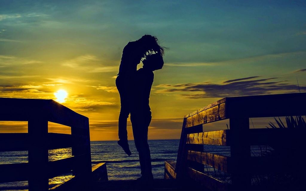 Gambar siluet romantis pasangan di pelabuhan saat matahari terbenam.