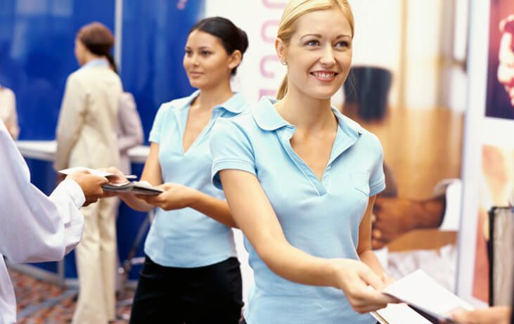Tiga orang wanita memegang dokumen dalam acara promosi percetakan.