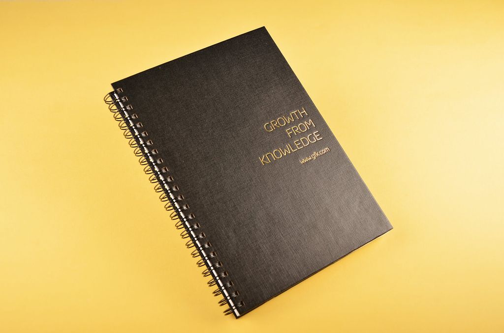 Buku spiral hitam dengan judul 'Growth from Knowledge' dan website www.gfk.com