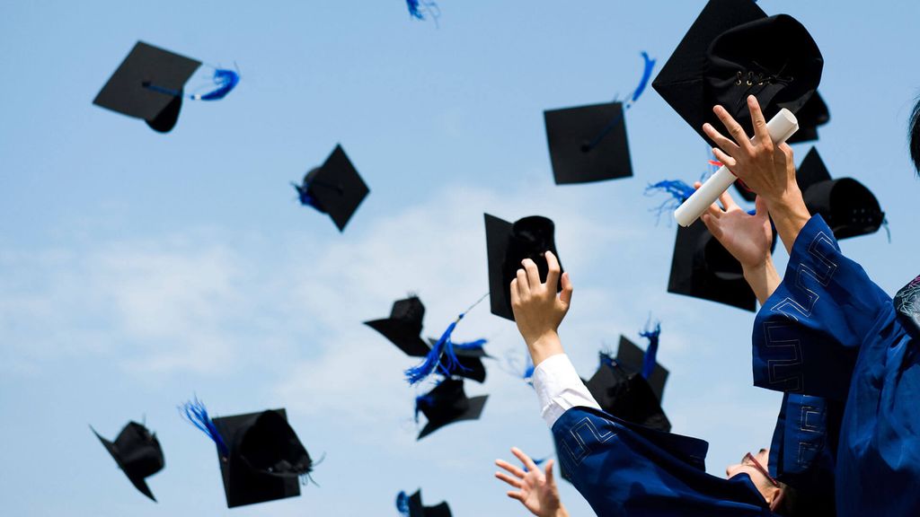 Para wisudawan melempar topi mereka ke udara dalam perayaan wisuda.
