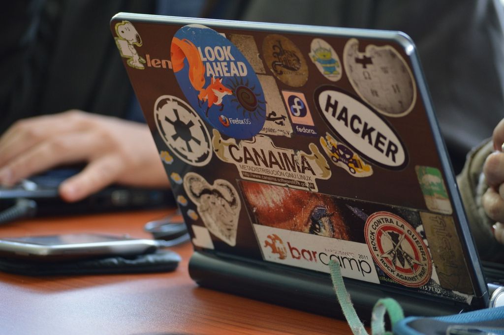 Tampilan laptop dengan berbagai stiker menarik, termasuk 'Hacker' dan 'Look Ahead'.