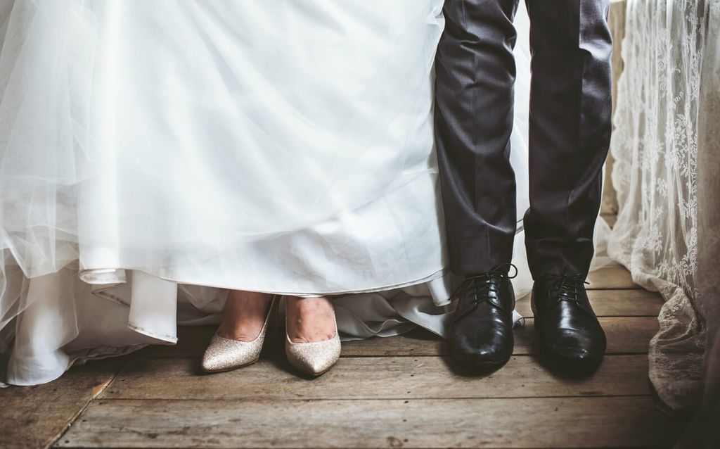 Kaki pengantin perempuan dan laki-laki berdiri di atas lantai kayu