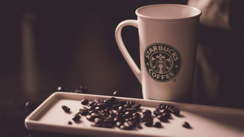 Cangkir Starbucks putih dengan logo hijau dan biji kopi hitam di meja.