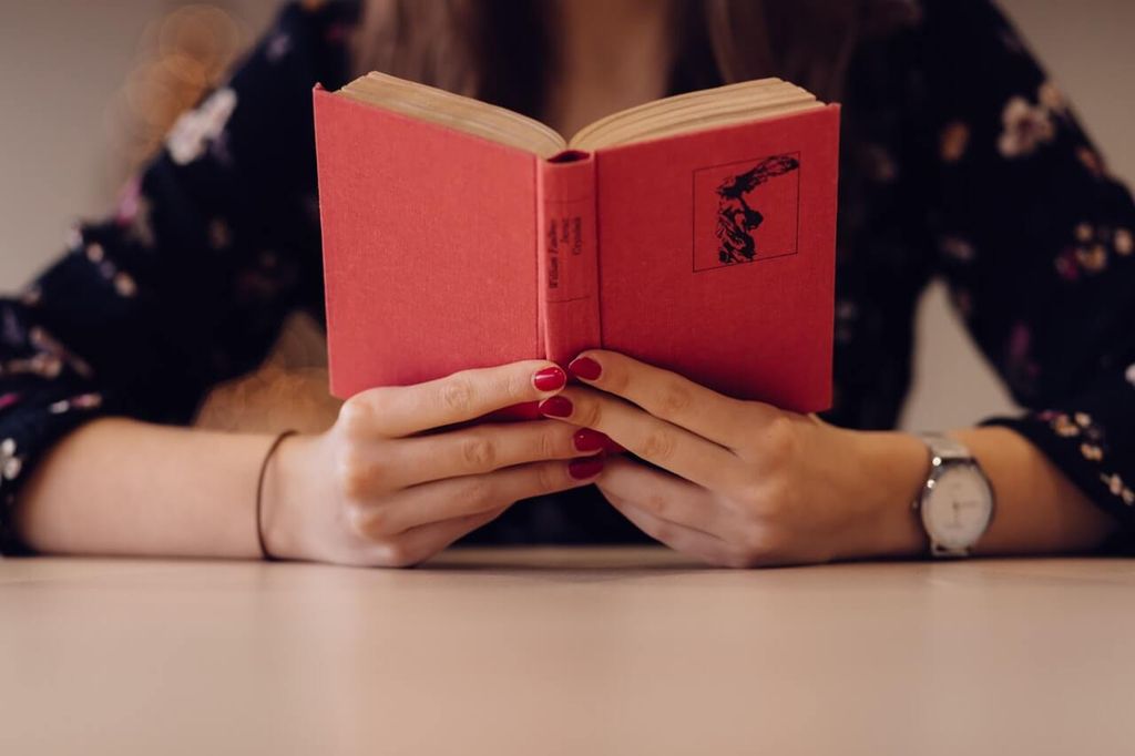 Tangan memegang buku merah dengan desain unik di halaman belakang.