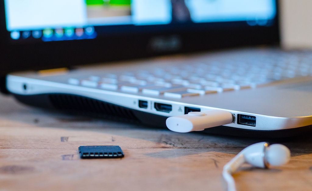 Laptop dengan perangkat eksternal dan aksesori di meja kayu.
