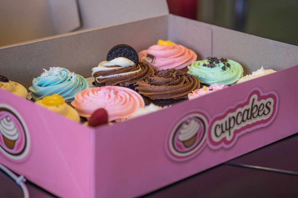 Kotak cupcakes berwarna pink dengan berbagai topping lezat dan berwarna cerah.