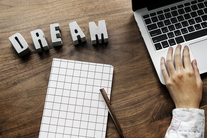 Tulis 'Dream' dengan huruf kayu di meja, laptop, dan buku catatan.