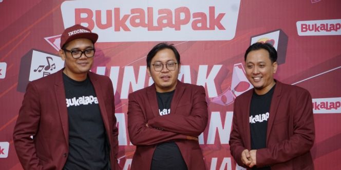 Tiga orang berpose depan backdrop merah dengan logo Bukalapak dan Uprint.id