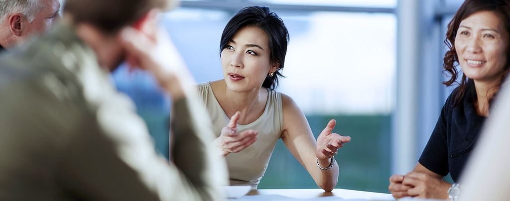 Tiga orang sedang berbicara dalam pertemuan bisnis, fokus pada wanita yang berbicara.