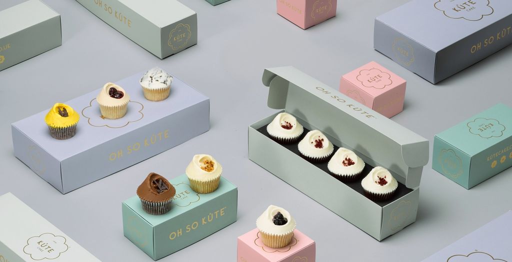 Paket cupcake 'Oh So Küte' dalam kotak berwarna pastel, menampilkan variasi topping dan bentuk.