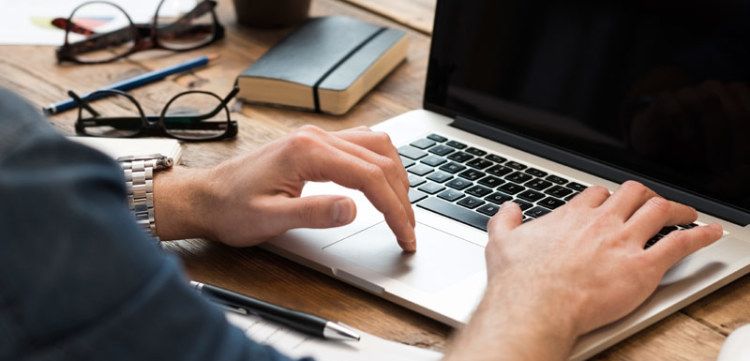 Tangan sedang mengetik di laptop di meja kerja.
