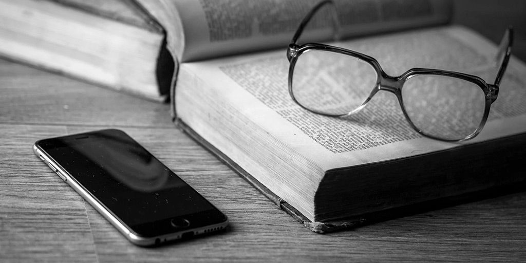 Buku terbuka dengan kacamata dan smartphone di meja kayu, konsep belajar atau kerja.