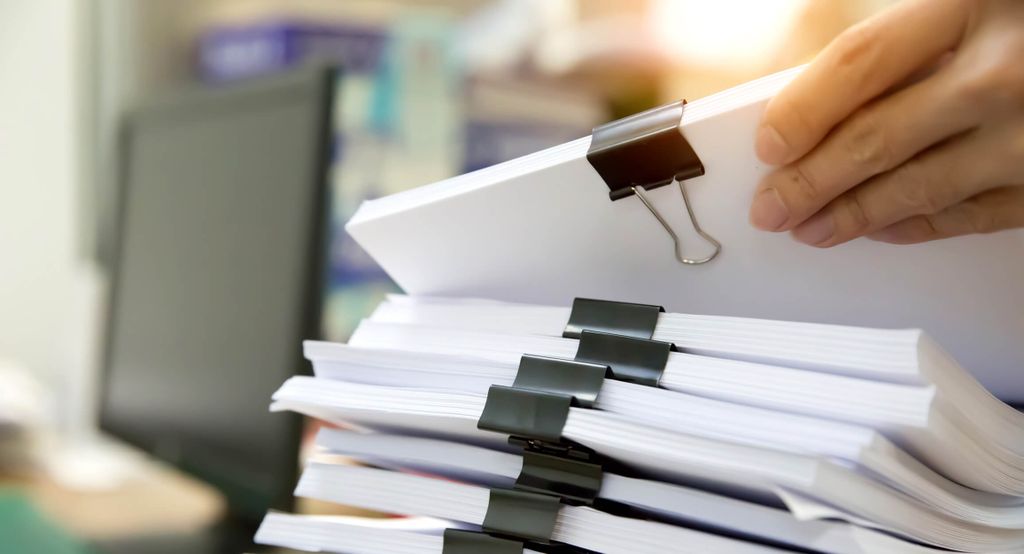 Stack of documents being held by a hand with a binder clip attached.