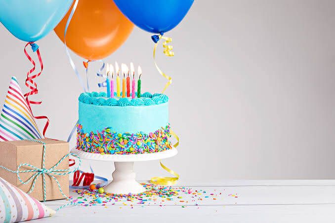 Tart ulang tahun berwarna biru dengan lilin dan balon, cocok untuk perayaan.