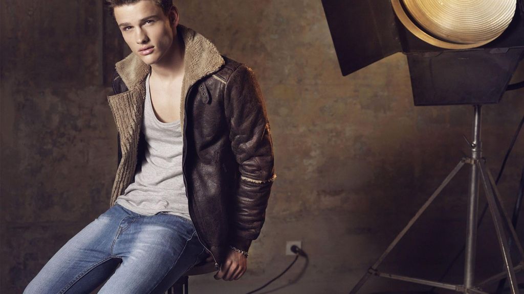 Pria muda memamerkan jaket kulit dan celana jeans di studio foto.