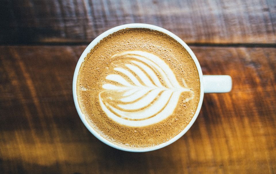 Cangkir cappuccino dengan latte art berbentuk daun di atas meja kayu untuk ilustrasi aktivasi sampel coffee shop baru