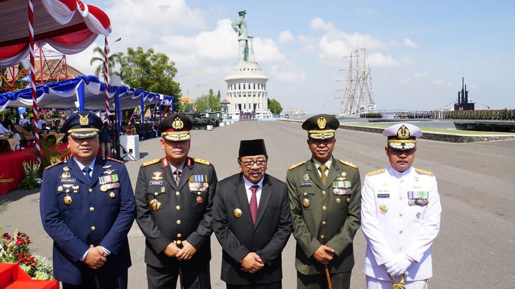 Grup personel militer berpose di depan lapangan dengan latar patung dan kapal layar.