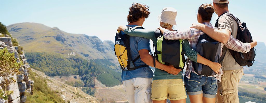 Empat orang dengan ransel di puncak gunung, menikmati pemandangan indah.