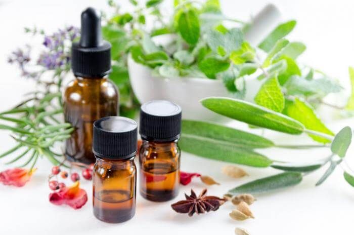 Tiga botol minyak atsiri berwarna cokelat dengan tumbuhan herbal di sekitarnya.