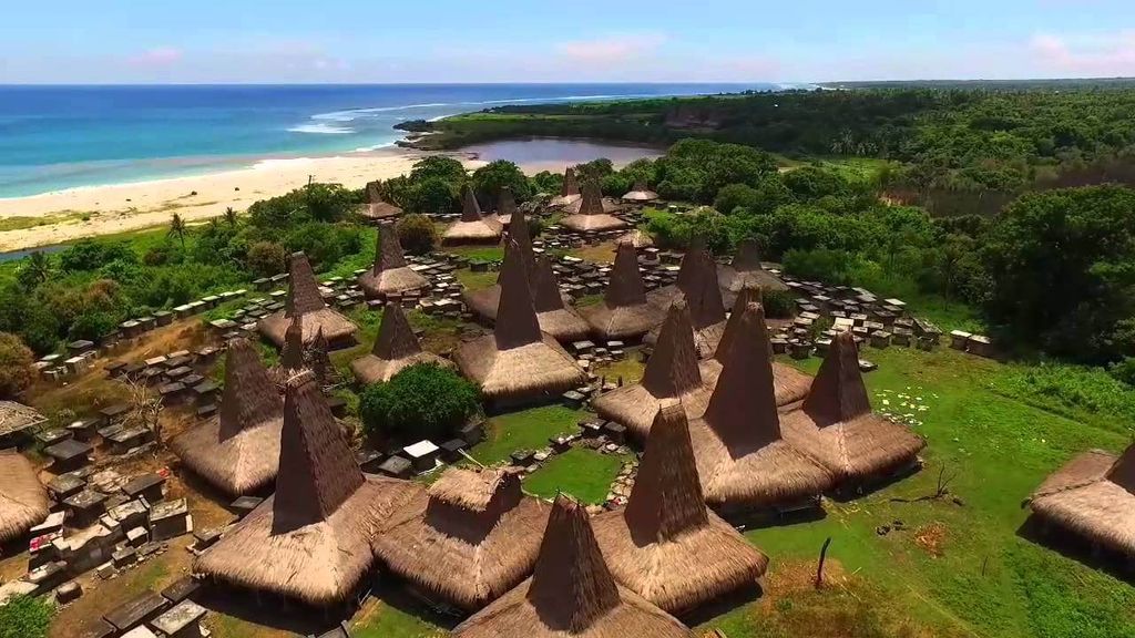 Pemandangan desa adat tradisional dengan atap rumah-rumah datar di tepi pantai yang hijau dan biru.