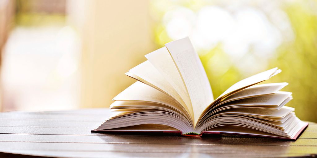 Buku terbuka dengan halaman putih di meja kayu, latar belakang bokeh hijau.
