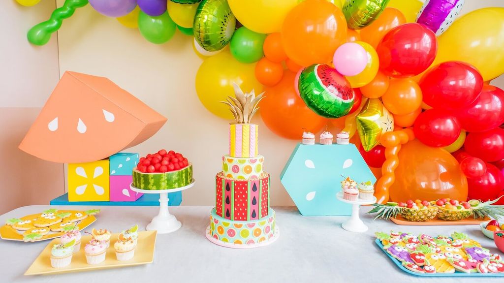 Meja pesta dengan kue bertema buah dan balon warna-warni