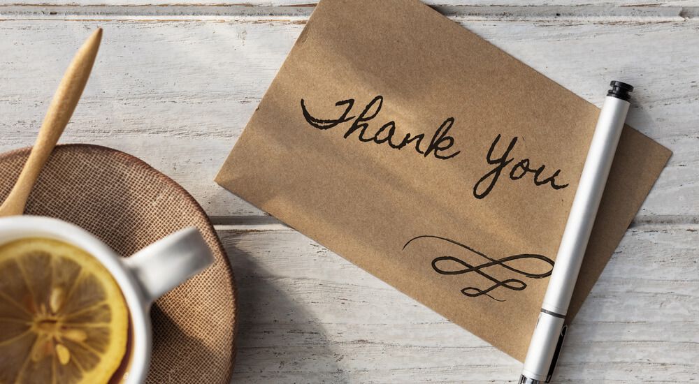 Kartu terima kasih bertuliskan 'Thank You' di atas meja kayu putih.