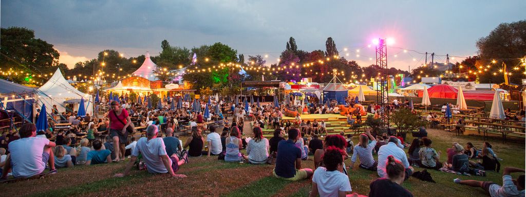 Pemandangan malam festival dengan penonton dan panggung di depan tenda.