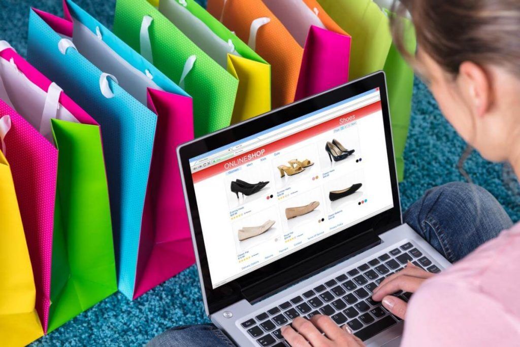 Seorang wanita membeli sepatu online di laptop sambil membandingkan pilihan barang preloved untuk bisnis jual beli barang bekas