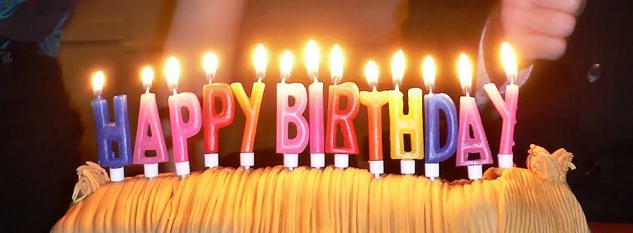 Kue ulang tahun dengan lilin huruf 'HAPPY BIRTHDAY' yang sedang terbakar