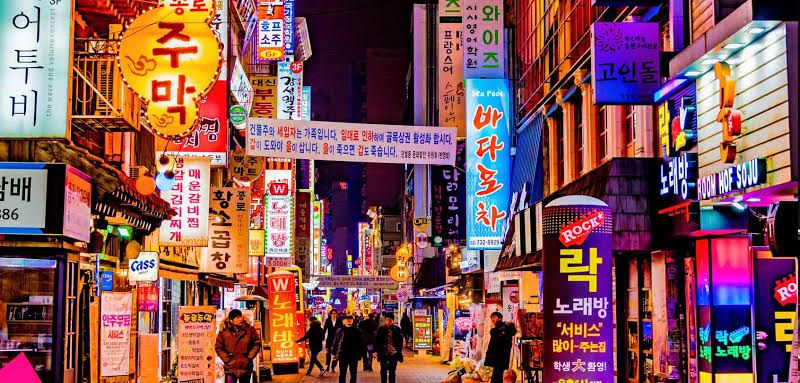 Pemandangan malam kota dengan berbagai lampu neon dan penanda iklan berbahasa Korea.