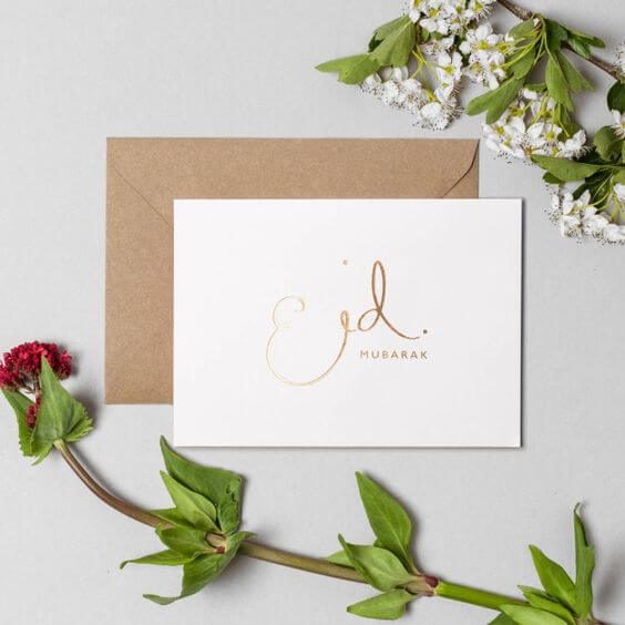 Ucapan Eid Mubarak elegan dengan tulisan emas dan bunga putih di sekelilingnya.