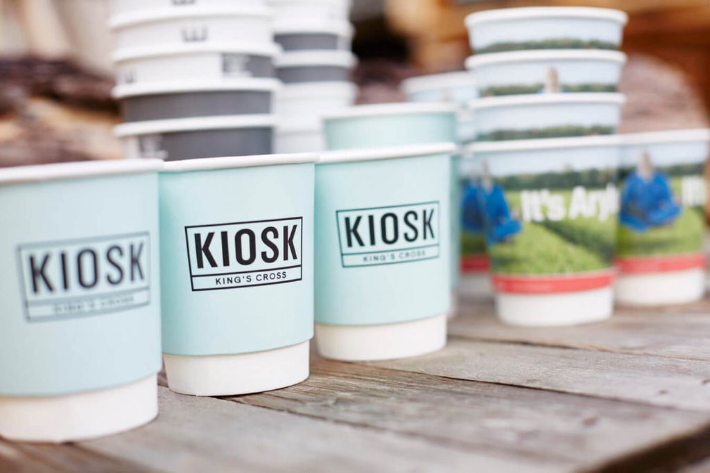 Paper cups with 'KIOSK' branding on a wooden surface.