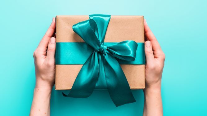 Tangan memegang kotak hadiah bertali biru di latar biru