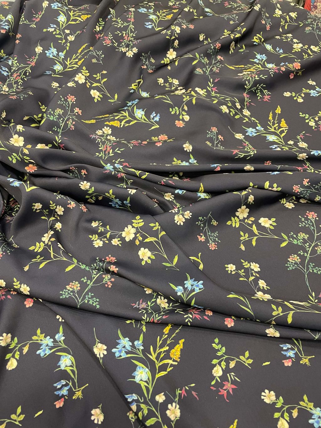 Gambar kain dengan motif bunga kecil berwarna-warni di atas latar hitam.