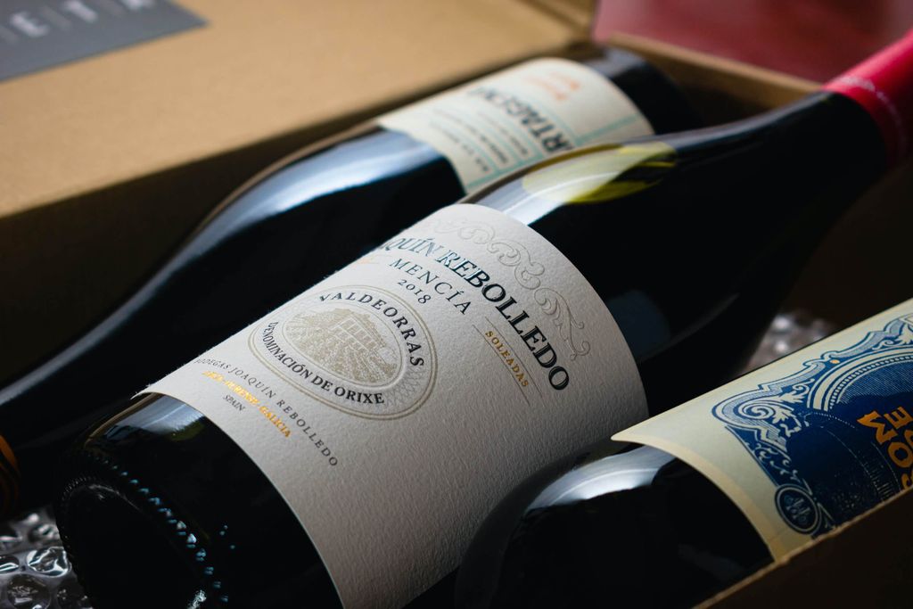 Gambar botol wine dengan label dekat dan kemasan hitam di belakang.