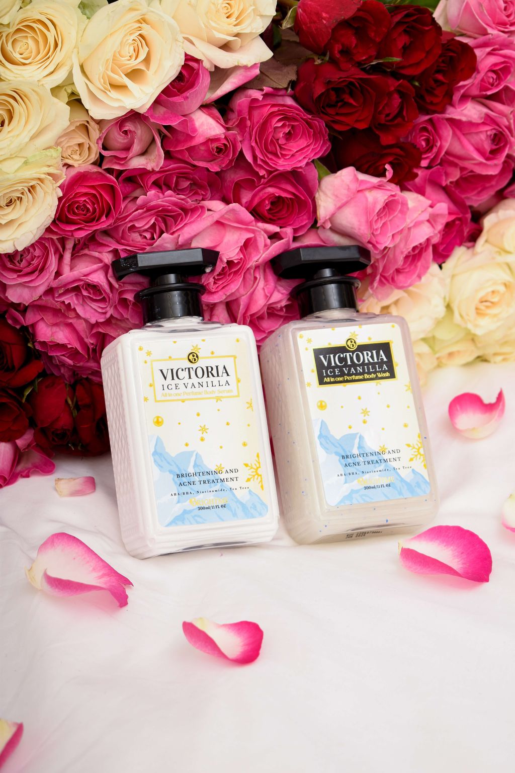 Dua botol sabun cair Victoria Secret di antara bunga mawar merah dan putih.