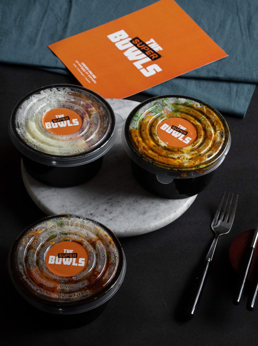 Tiga bowl makanan dengan label 'The Bowls' di atas meja hitam.