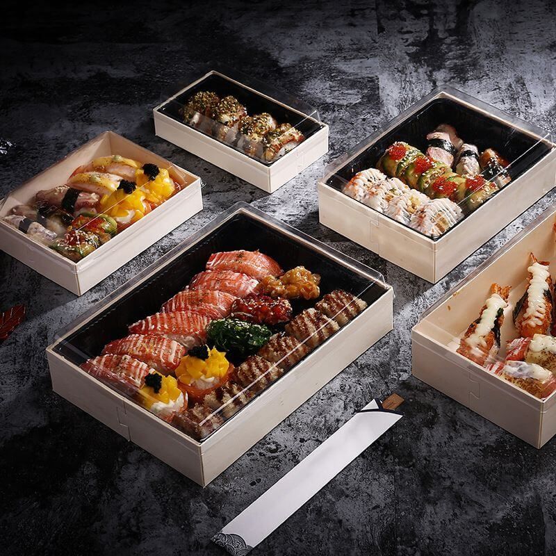 Pilihan makanan sushi dalam kotak plastik berwarna putih dan hitam, siap dikirim.