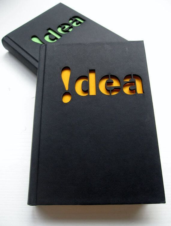 Buku hitam dengan logo 'Idea' berwarna kuning dan hijau, menunjukkan desain modern dan profesional.