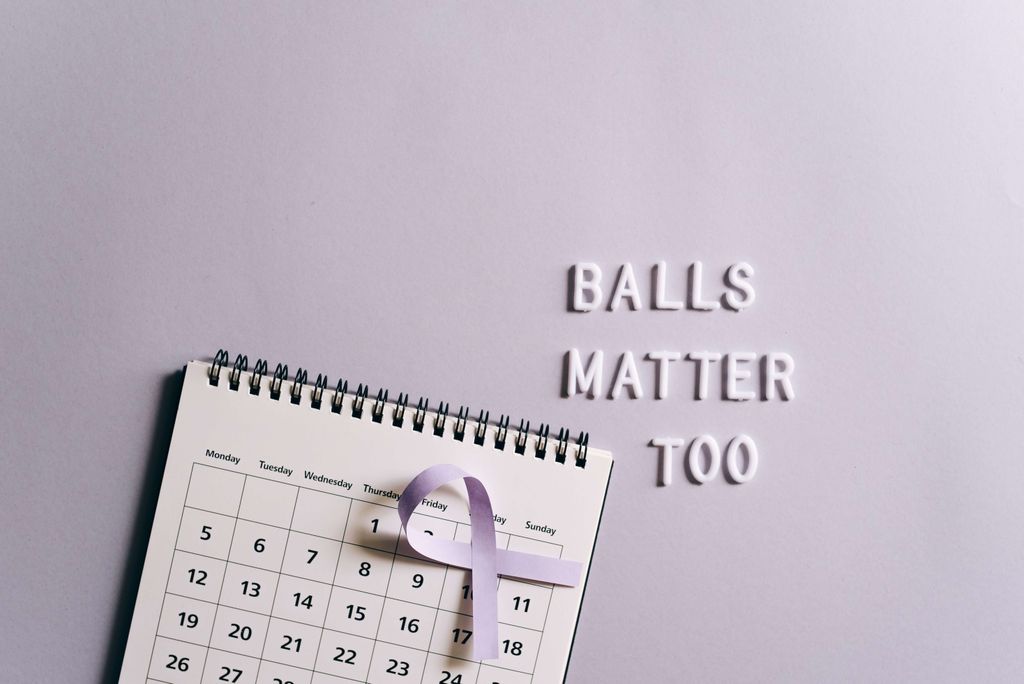 Kalender dengan ribbon ungu dan tulisan 'BALLS MATTER TOO' untuk kampanye kanker payudara.