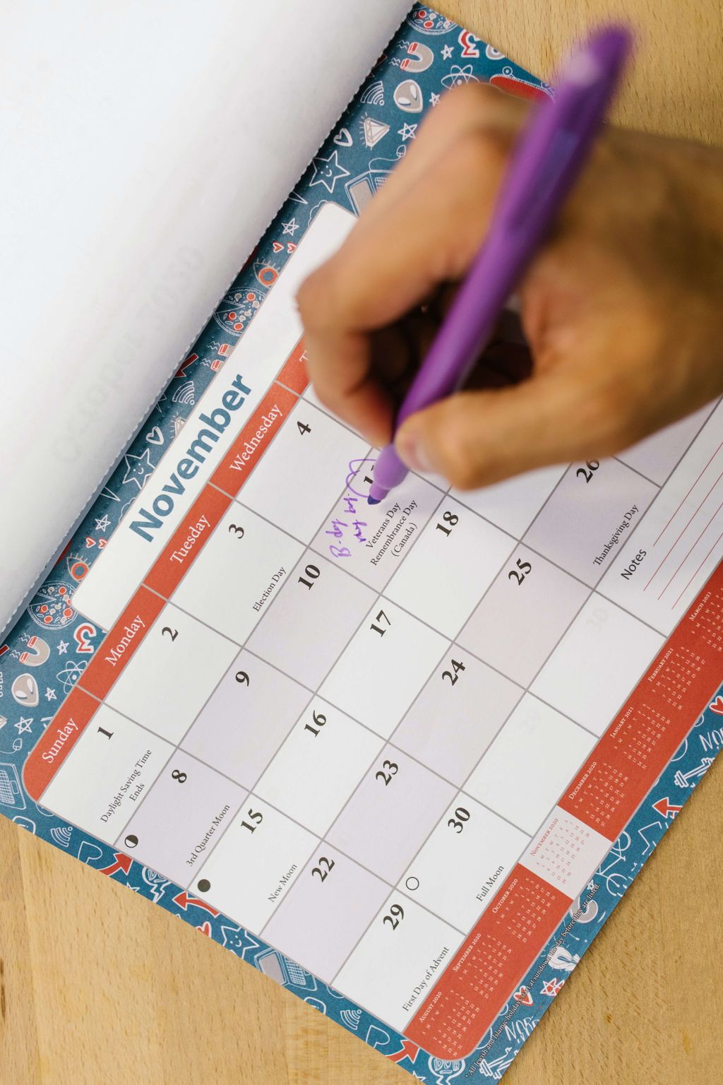 Tangan menulis tanggal di kalender bulan November dengan pulpen ungu.