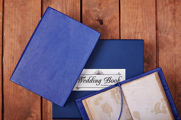 Buku wedding biru dengan label 'Wedding Book' di atas meja kayu.