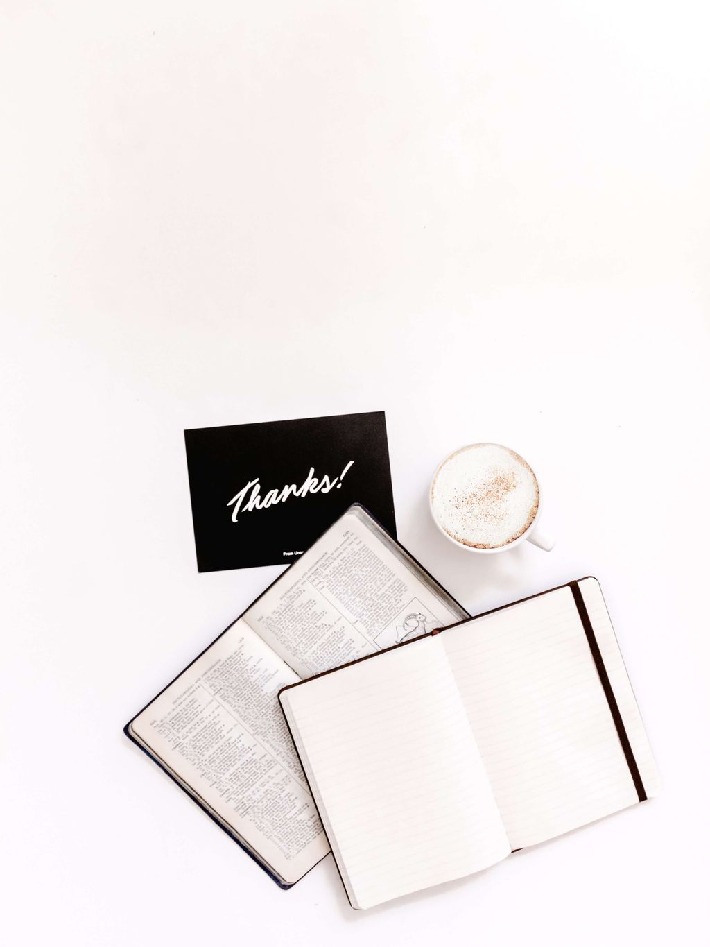 Buku terbuka, kopi, dan kartu 'Thanks' di meja putih.