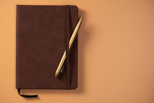 Notebook hitam dengan pulpen emas di atas latar cokelat.