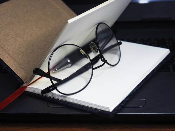 Buku, kacamata, dan pena di atas laptop, ideal untuk konten kerja atau pendidikan.