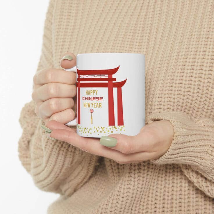 Tangan memegang mug putih dengan desain torii dan ucapan Happy Chinese New Year
