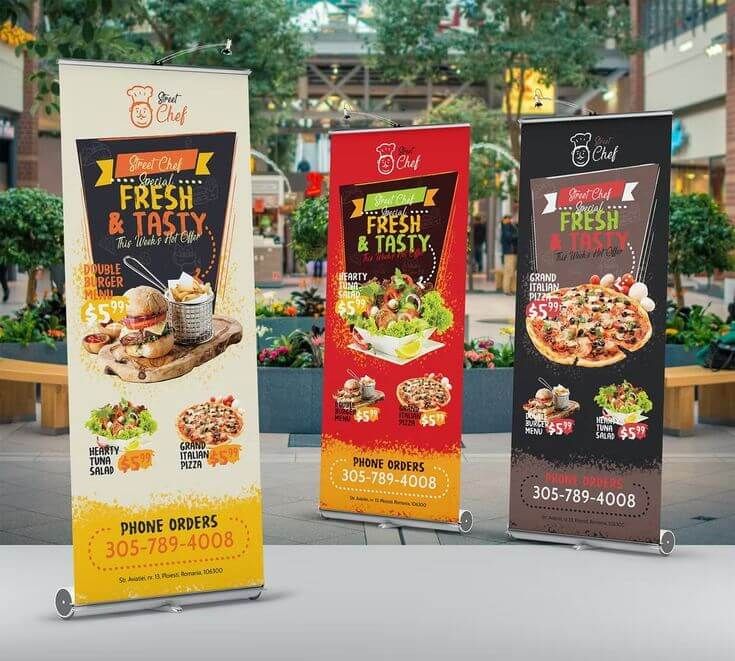 Tiga roll-up banner promosi makanan dari Uprint.id di area outdoor.