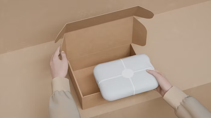 Tangan memasukkan kotak putih ke dalam kotak kraft terbuka.